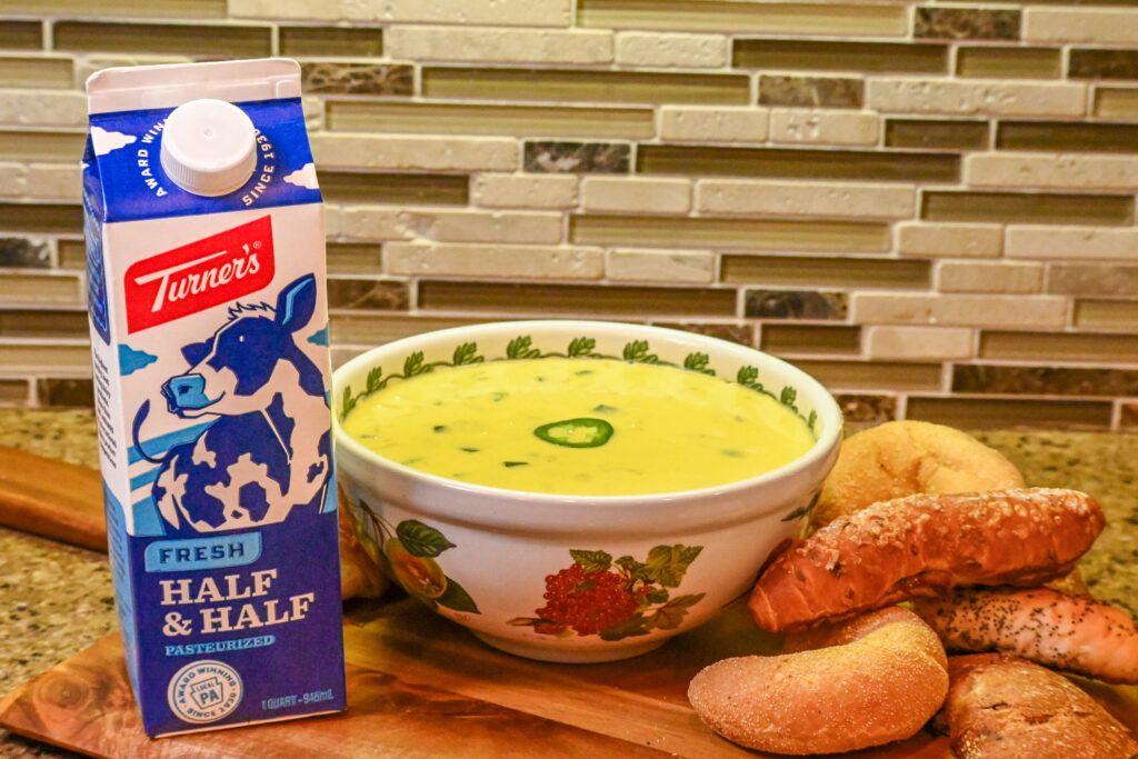 Quart of Turner's Half & Half next to a bowl of cheese sauce and bread on a kitchen counter.