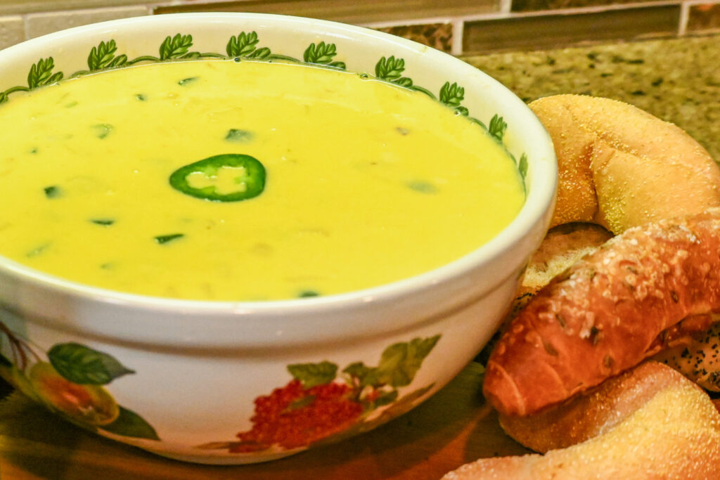 A bowl of cheese dip sits on a kitchen counter with bread sitting next to it.