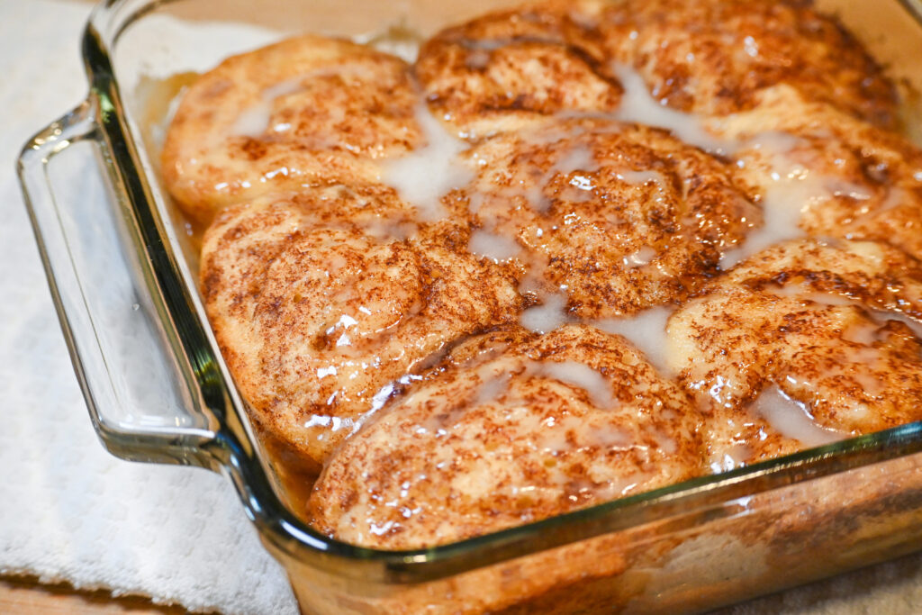 Cinnamon Rolls in a clear baking dish on a kitchen towel on the counter.