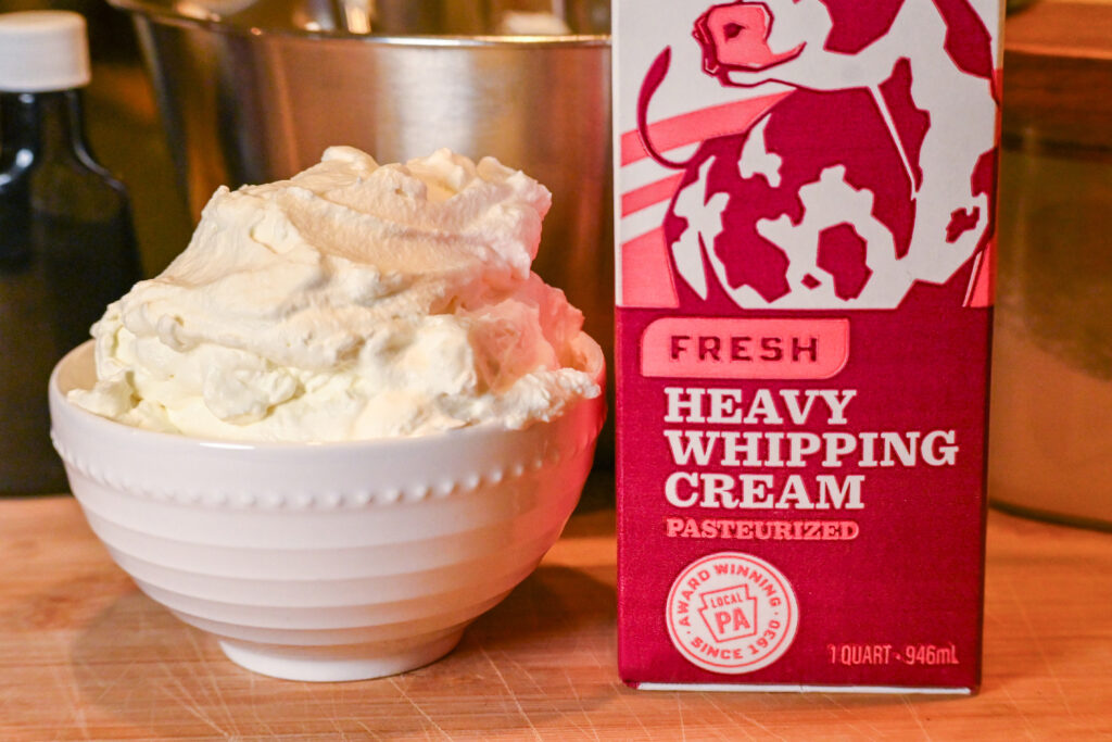 A close up image of a quart of Turner's Heavy Cream next to a bowl of  whipped cream with various kitchen items in the background.