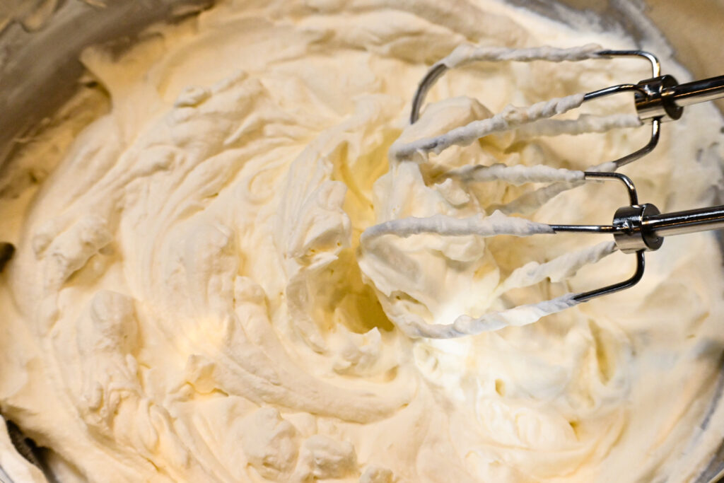 A bowl of whipped cream with two mixing whisks in the corner of the frame.